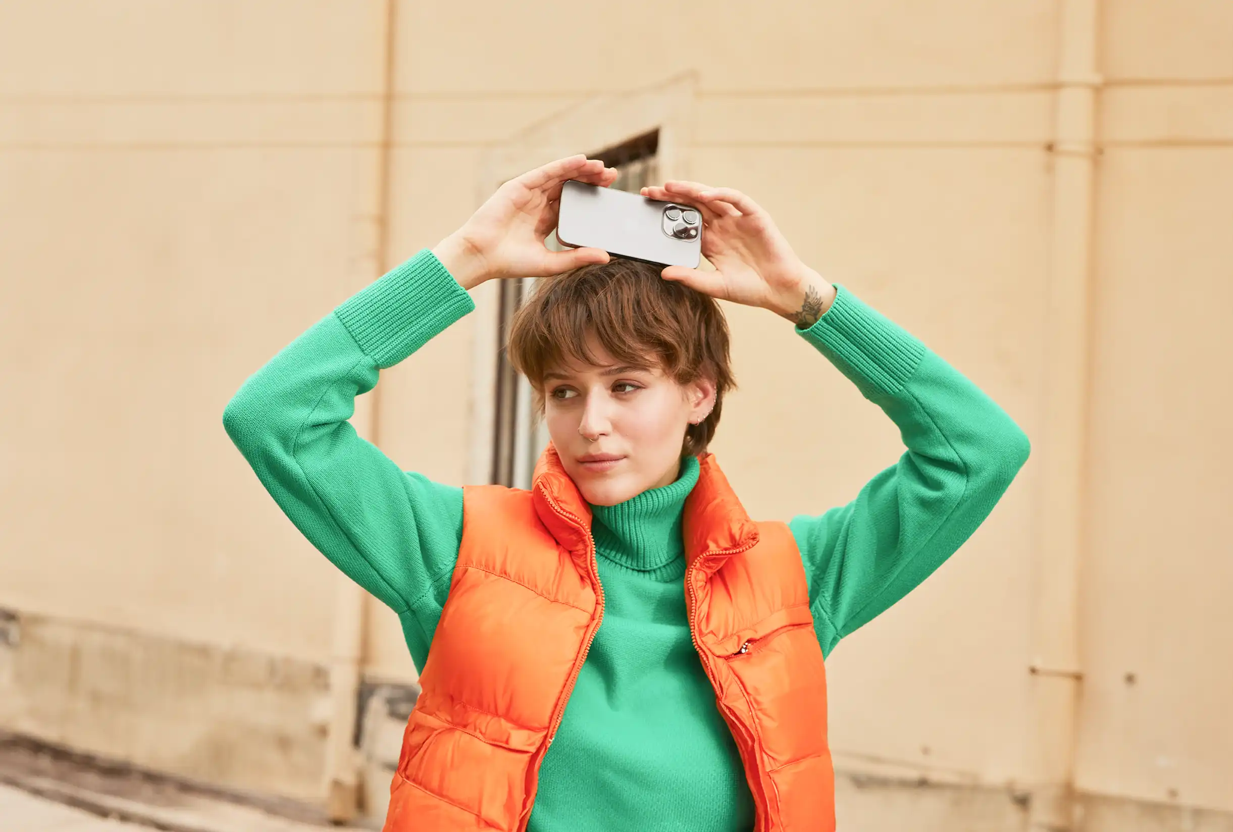 Women with a green pullover and an orange sleeveless jacket who held up her phone above her head